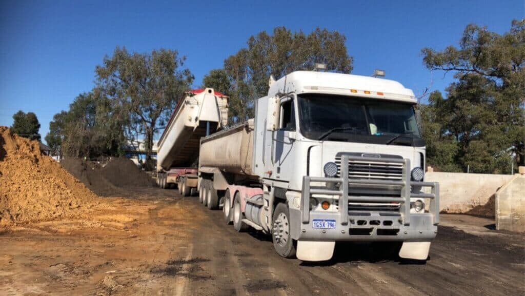 A large double white truck with a double dump body, the back dump body is in the process of offloading