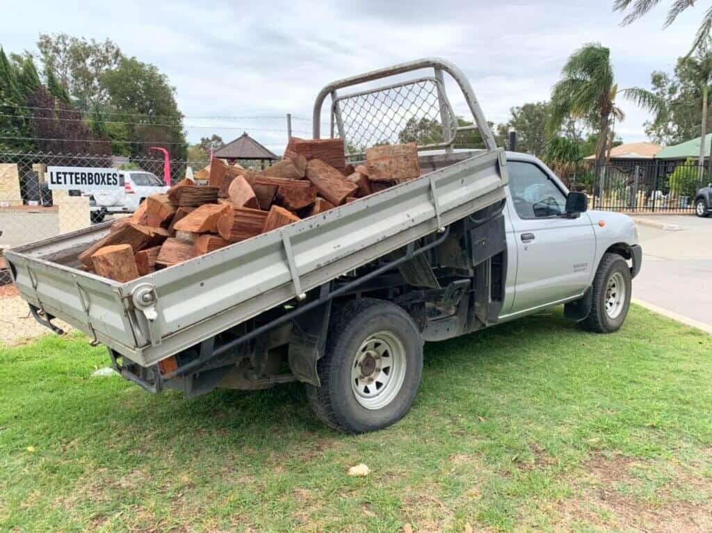 A tippy truck offloading whole pieces of wood, the truck is parked on grass